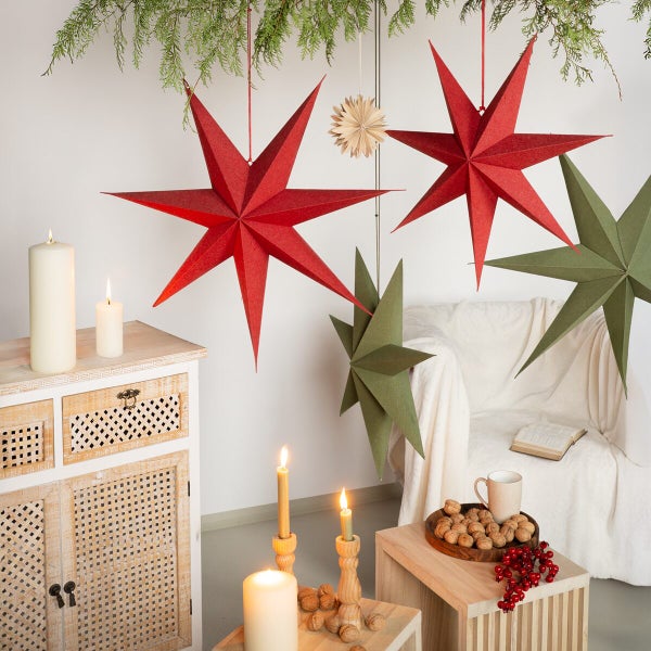 Weihnachtliche Szene mit hängenden Papiersternen in rot und grün, sowie Kerzen, Nüssen und einem gemütlichen Sessel für eine festliche Stimmung.