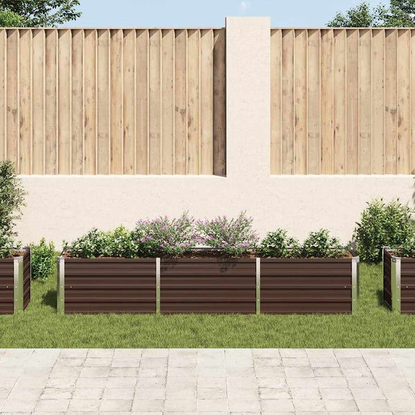 Rechteckiges Hochbeet aus Metall in einem Garten vor einem Holzzaun mit Blumen und Pflanzen bepflanzt.