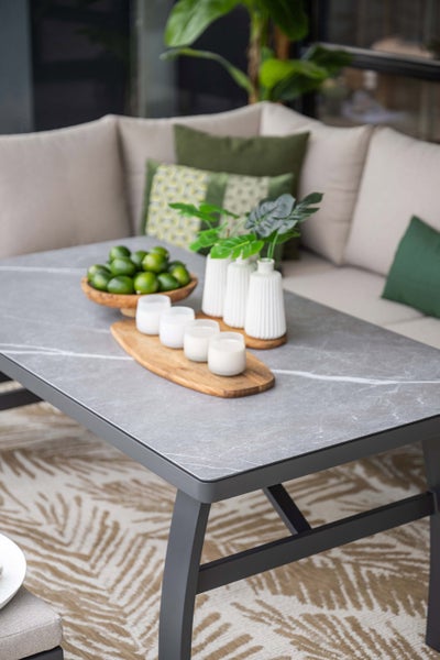 Grauer Garten-Loungetisch mit Tischplatte in Marmor-Optik, dekoriert mit Vasen und Schalen, vor einem Lounge-Sofa mit Kissen.