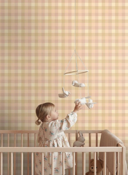 Vliestapete mit Vichy-Karomuster in einem hellen Kinderzimmer hinter einem hölzernen Gitterbett mit Mobile.