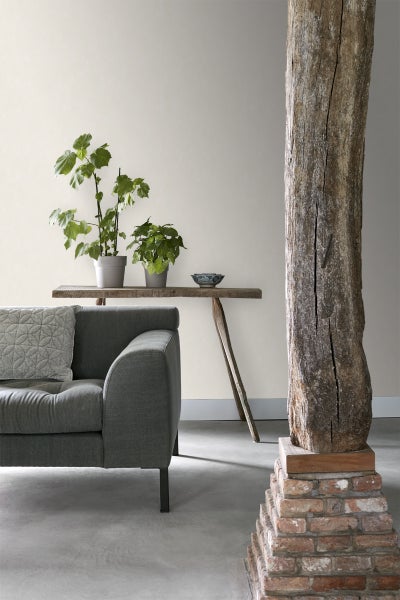 Wohnzimmer mit grauem Sofa, Holztisch mit Pflanzen und dekorativer Holzsäule auf einem Ziegelsteinsockel