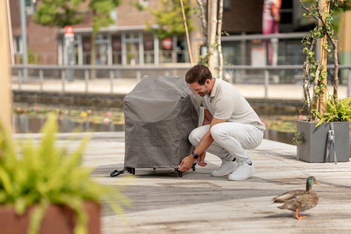 Mann befestigt eine Schutzhülle an einem Grill im Freien.