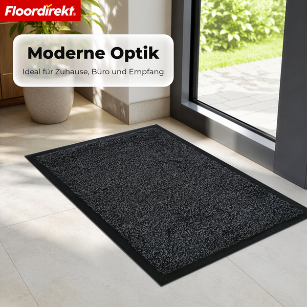 Moderne Floordirekt Fußmatte in einem hellen Eingangsbereich vor einer Glastür mit Blick in den Garten. Floordirekt Logo.
