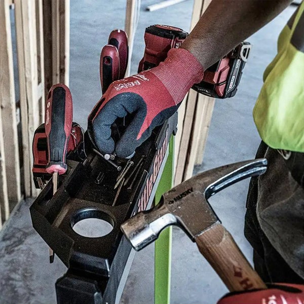 Handwerker mit Handschuhen greift Nägel aus einer schwarzen Werkzeugablage an einer Leiter bei der Arbeit auf einer Baustelle.
