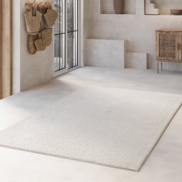 Hellbeiger, rechteckiger Teppich in einem hellen, minimalistisch eingerichteten Raum mit Holzmöbeln und Betonboden.
