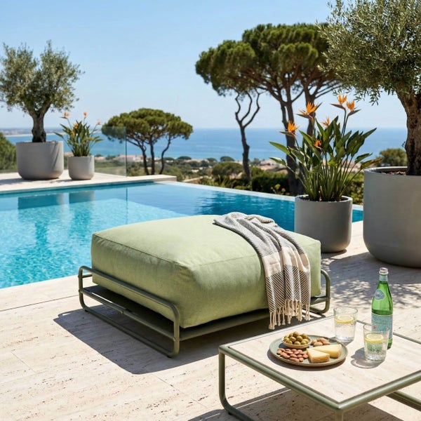 Moderner Outdoor-Loungebereich mit grünem Bodenkissen auf Metallrahmen am Pool, passendem Beistelltisch, großen Pflanzgefäßen und Meerblick.