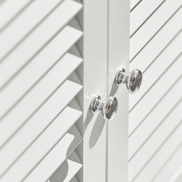 Detailaufnahme eines weißen Schranks mit Lamellentüren und runden, silberfarbenen Griffen.