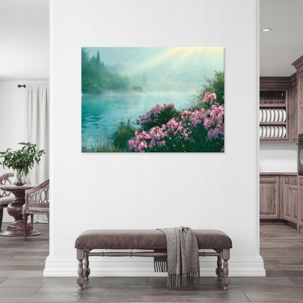 Wandbild mit einer Naturlandschaft, ein See mit Blumen und Bergen, aufgehängt an einer weißen Wand über einer Sitzbank mit einer Wolldecke.