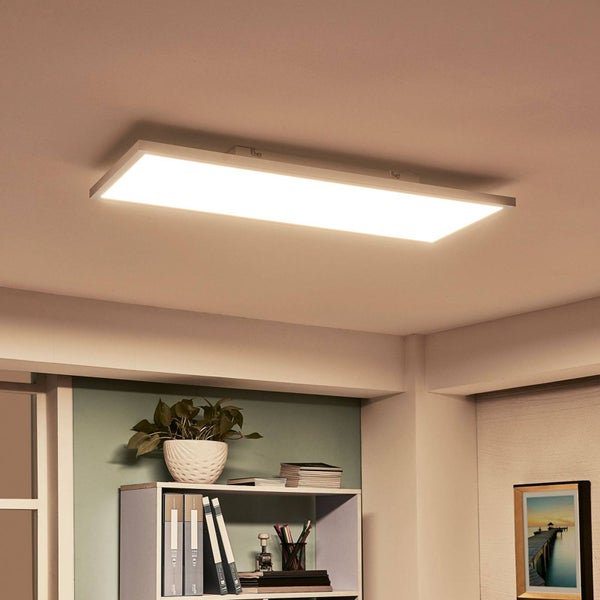 Moderne rechteckige LED-Deckenleuchte in einem hellen Arbeitszimmer über einem Regal mit Pflanze und Aktenordnern.
