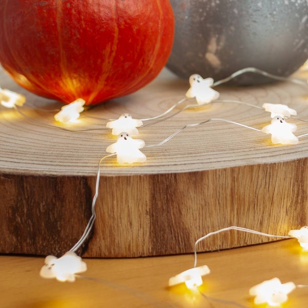 LED-Lichterkette mit kleinen weißen Gespenstern an Silberdraht, dekoriert auf einer Holzscheibe mit einem Kürbis, Halloween-Dekoration.