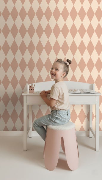 Mädchen sitzt an einem Schreibtisch vor einer Wand mit Rautenmuster.