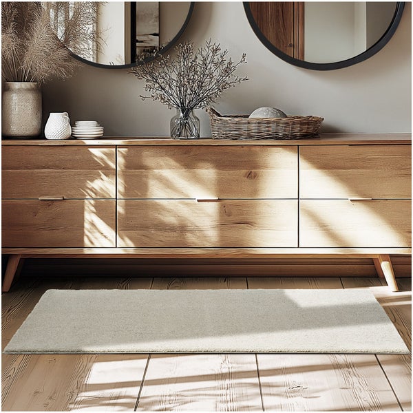 Heller, rechteckiger Teppich auf einem Holzboden vor einer Kommode aus Holz. Heller und moderner Einrichtungsstil.