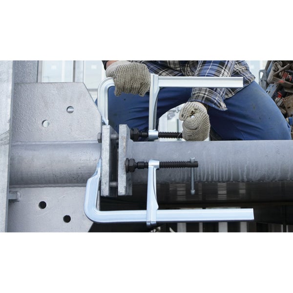 Person befestigt Rohr mit Schraubzwingen.