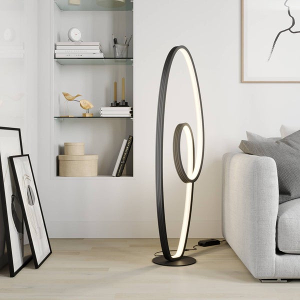 Moderne LED-Stehleuchte in Spiralform neben einem Sofa in einem hellen, organisierten Wohnzimmer mit Einbauregal.