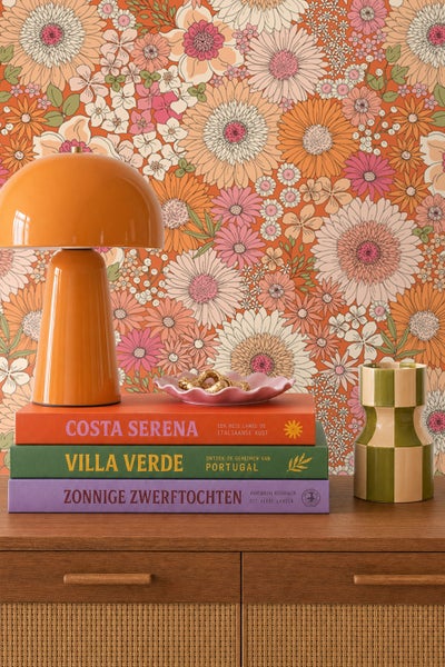 Wohnraumgestaltung mit Retro-Blumentapete, Tischleuchte, Büchern und Vase auf einem hölzernen Sideboard.