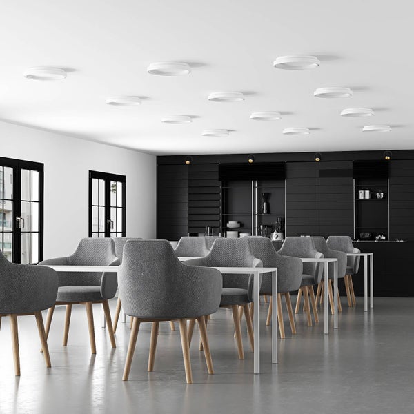 Heller, moderner Raum mit runden, weißen Deckenleuchten, grauen Polsterstühlen und weißen Tischen vor einer schwarzen Küchenwand.