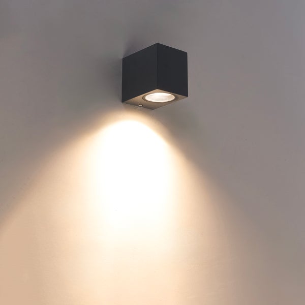 Würfelförmige Wandleuchte in Schwarz mit nach unten gerichtetem Lichtstrahl auf einer Wand.