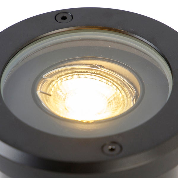 Runder LED Bodeneinbaustrahler aus schwarzem Metall mit leuchtender warmweißer Lichtquelle in der Nahaufnahme.
