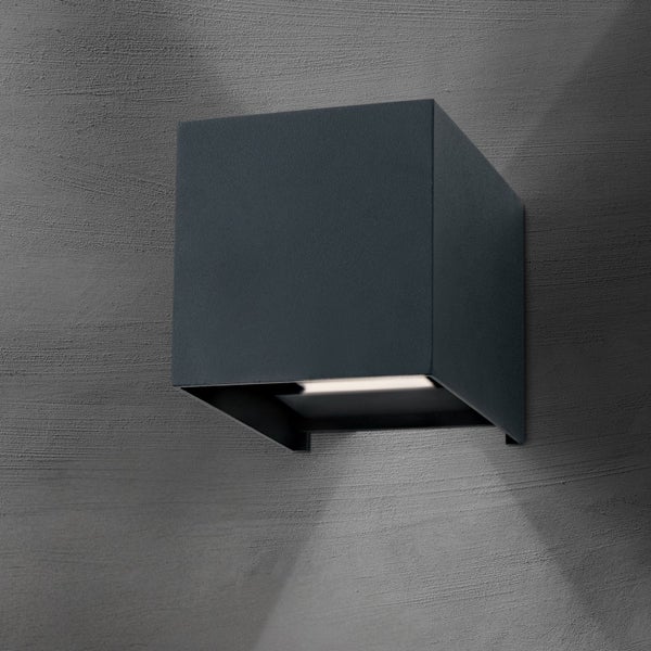 Würfelförmige Außenwandleuchte aus Metall mit nach unten gerichtetem Lichtstrahl auf einer strukturierten Wand.