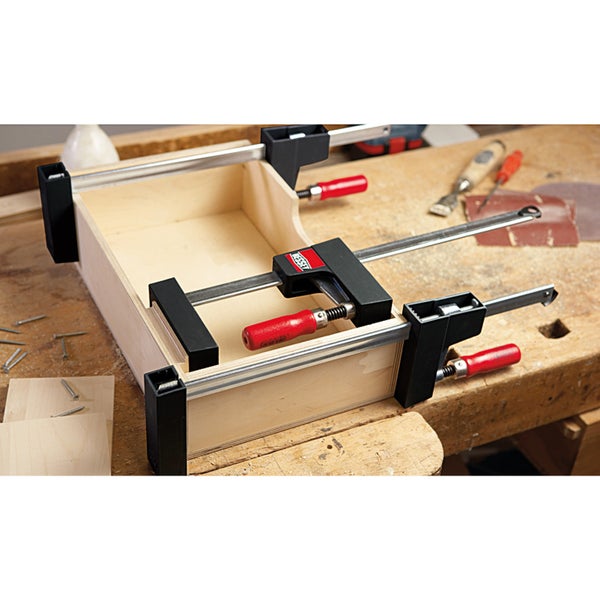 Bessey Korpuszwingen fixieren einen Holzkasten auf einer Werkbank mit Werkzeugen und Holzspänen.