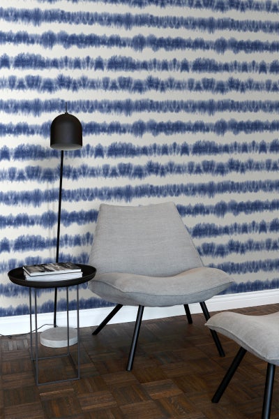 Zimmer mit gemusterter Tapete, Sessel, Fußhocker und Beistelltisch