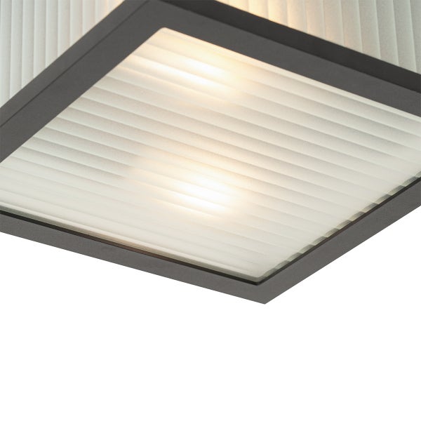 Nahaufnahme einer Leuchte mit Metallrahmen und geriffeltem satiniertem Glas, beleuchtet.