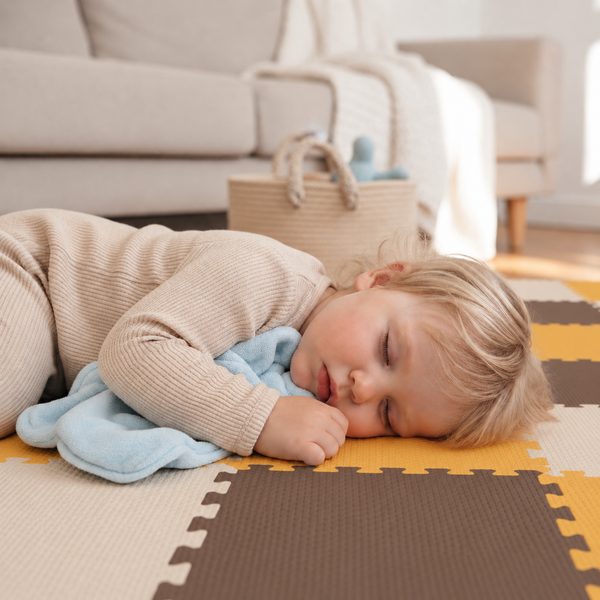 Ein Kleinkind schläft auf einer Puzzlematte aus Schaumstoff im Wohnzimmer mit einem Kuscheltuch.
