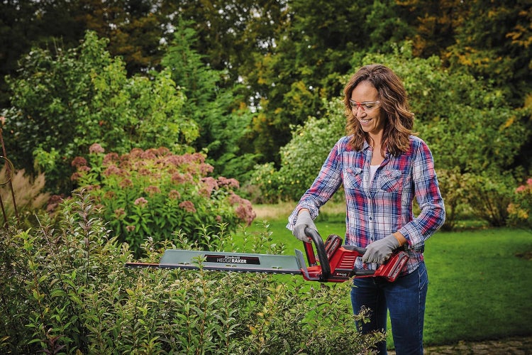 Frau schneidet eine Hecke mit einer akkubetriebenen Einhell Heckenschere inklusive Hedge Raker Aufsatz im Garten.