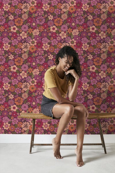 Frau sitzt vor einer Wand mit floralem Muster.