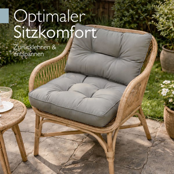 Gartenstuhl aus Rattan mit grauen Sitzkissen und Rückenpolster in einem sonnigen Garten auf einer Steinterrasse.