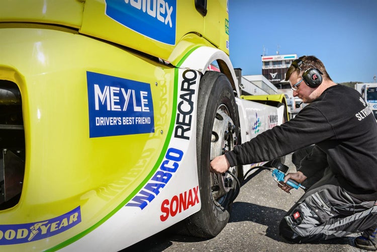 Ein Mechaniker füllt den Reifen eines Rennwagens mit Logos von Meyle, Wabco, Sonax und Recaro auf.