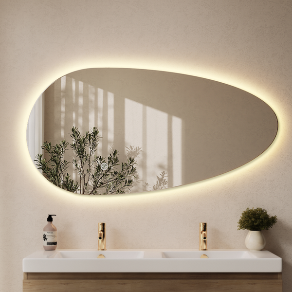 Organisch geformter Badezimmerspiegel mit indirekter LED-Beleuchtung über einem Doppelwaschtisch mit Holzunterschrank.