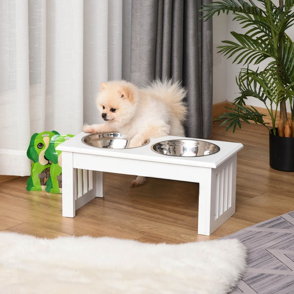 Erhöhte Futterstation für Hunde in Weiß mit zwei Edelstahlnäpfen in einem Wohnraum mit kleinem Hund.