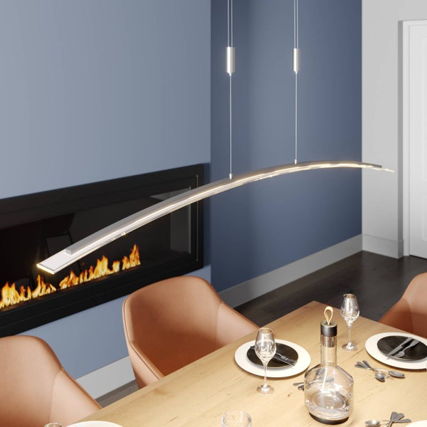 Moderne, gebogene LED-Pendelleuchte aus Metall über einem Holztisch in einem Esszimmer mit Kamin und blauen Wänden.