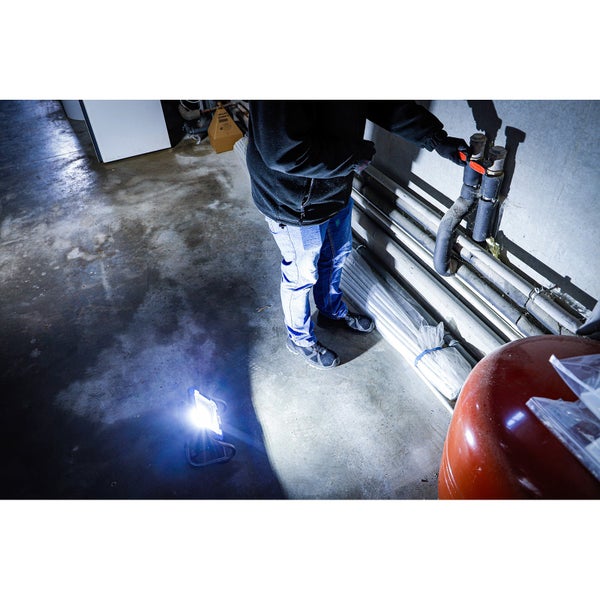 Eine Person arbeitet in einem Keller mit einer tragbaren LED-Arbeitsleuchte, um die Rohrleitungen zu inspizieren.