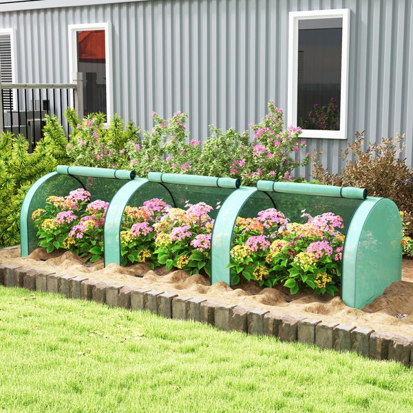 Folientunnel für Pflanzen im Garten vor einer Hauswand mit blühenden Blumenbeeten und einer Einfassung aus Steinpflaster.