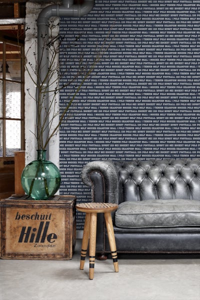 Dekoratives Interieur mit Sofa, Hocker und Vintage-Elementen vor gemusterter Tapete