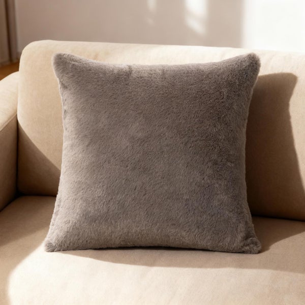 Quadratisches Dekokissen aus grauem Kunstfell auf einem Sofa.