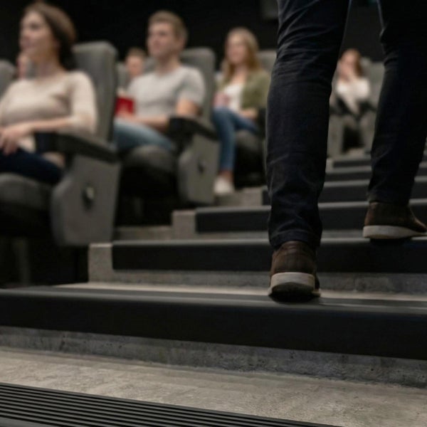 Person geht die Treppe in einem Kinosaal hinauf während andere Personen im Hintergrund auf ihren Sitzen den Film ansehen