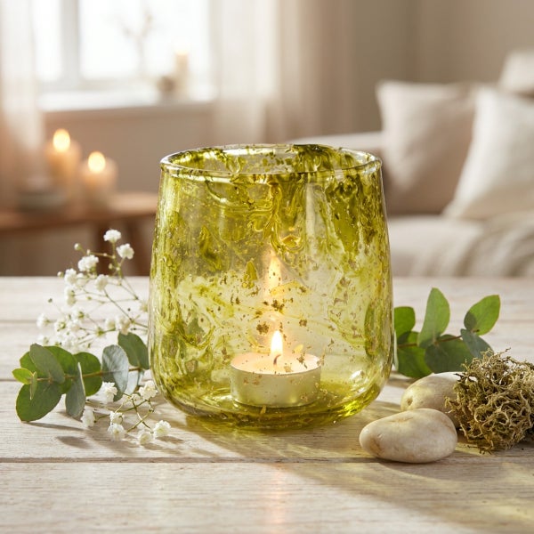 Dekoratives Windlicht aus Glas mit marmorierter Struktur auf einem Holztisch mit Dekoration aus Blumen, Eukalyptus und Steinen.