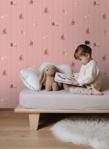 Kindertapete mit Tiermotiven und Streifenmuster in einem Kinderzimmer mit Kind auf einem Bett.