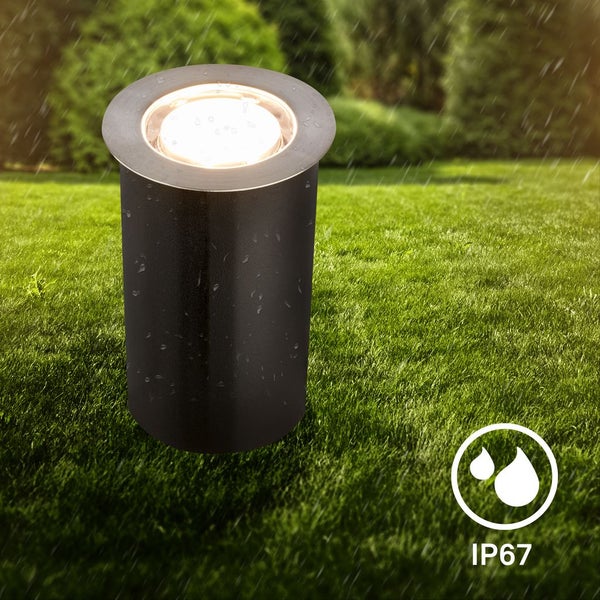 Zylindrische schwarze LED-Bodeneinbauleuchte aus Metall auf einer Rasenfläche im Regen mit Schutzart IP67.
