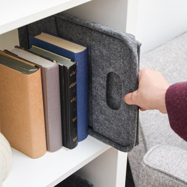 Hand zieht einen Filzkorb mit Griff aus einem weissen Regal neben mehreren Büchern.