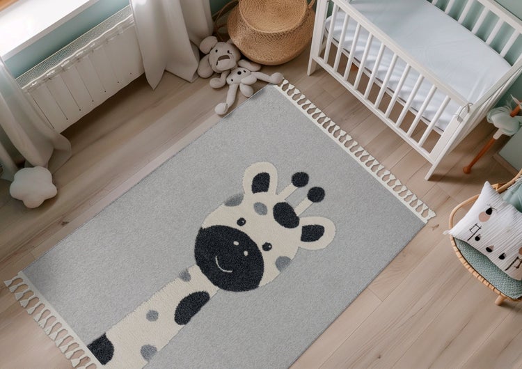 Kinderteppich mit Giraffenmotiv und Fransen in einem gemütlich eingerichteten Babyzimmer mit Gitterbett auf Holzboden.