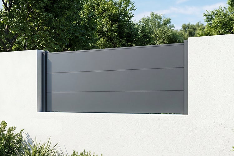 Moderner Sichtschutzzaun aus Metall mit waagerechten Lamellen montiert zwischen zwei weißen Mauerpfosten vor einer Gartenkulisse.