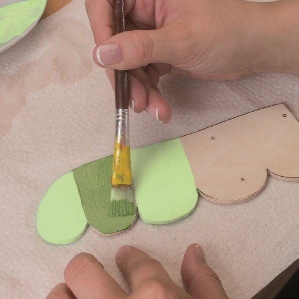 Eine Hand bemalt eine hölzerne Form mit einem Pinsel und Farbe