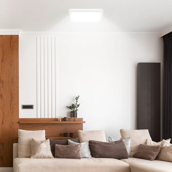 Moderne, quadratische LED-Deckenleuchte in einem hellen Wohnzimmer mit beigem Sofa und Wandverkleidung aus Holz.