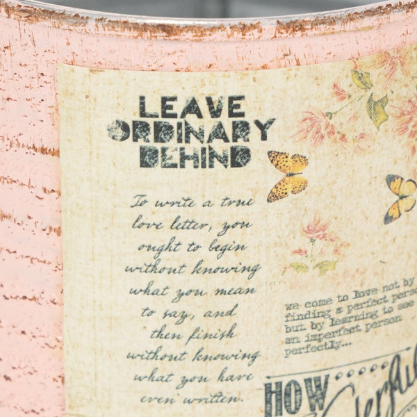 Nahaufnahme eines Deko-Metallbehälters im Vintage-Stil mit der Aufschrift Leave ordinary behind, Schmetterlingen und Blumenmotiven.