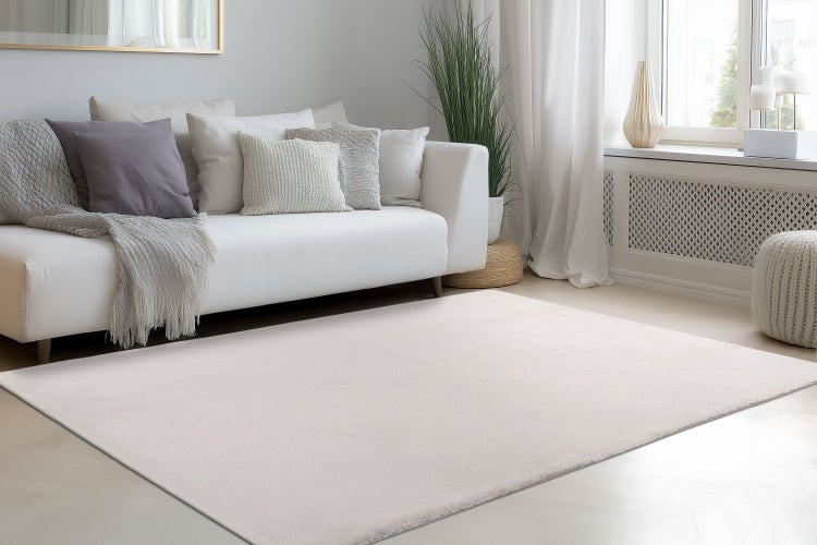 Ein unifarbener Teppich in einem modern eingerichteten Wohnzimmer mit Sofa, Zierkissen und hellem Boden.