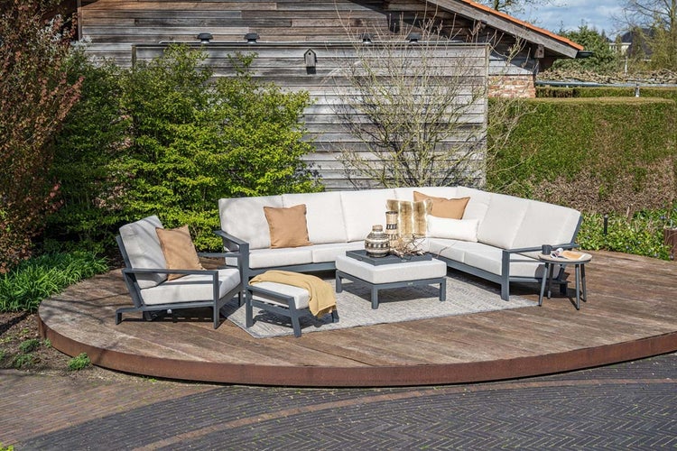 Modernes Garten-Lounge-Set mit Ecksofa, Sessel, Hocker und Beistelltisch auf einer runden Holzterrasse mit hellen Polstern und Metallrahmen.